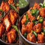 Crispy restaurant-style Paneer 65 garnished with fried curry leaves, green chillies, and lemon wedges.